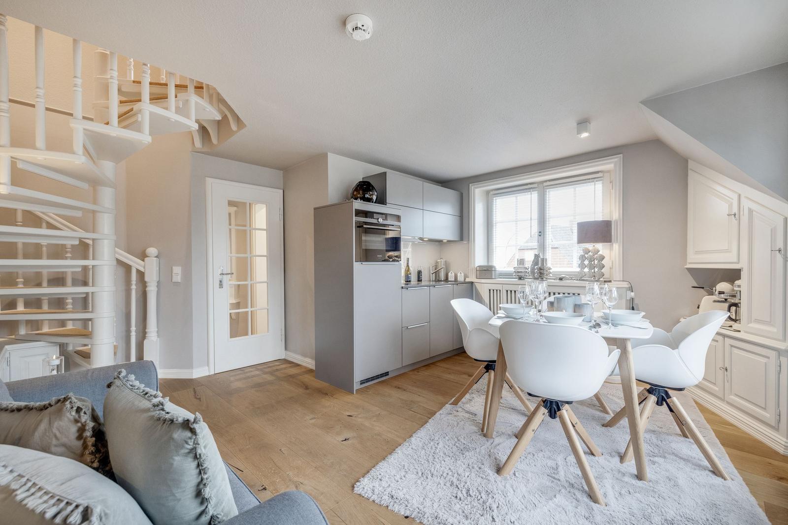Küche mit Essbereich, weiße Stühle, Spindelstiege und Holzboden.