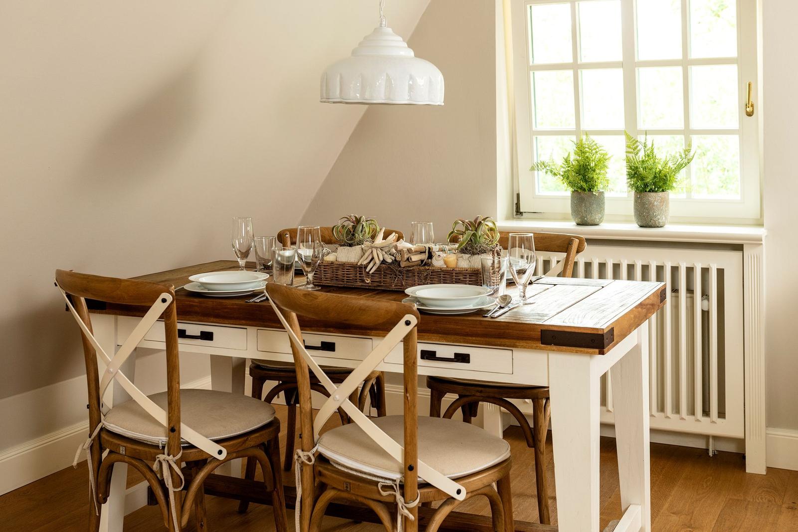 Esszimmer mit Holztisch, Stühlen und Fenster mit Pflanzen.