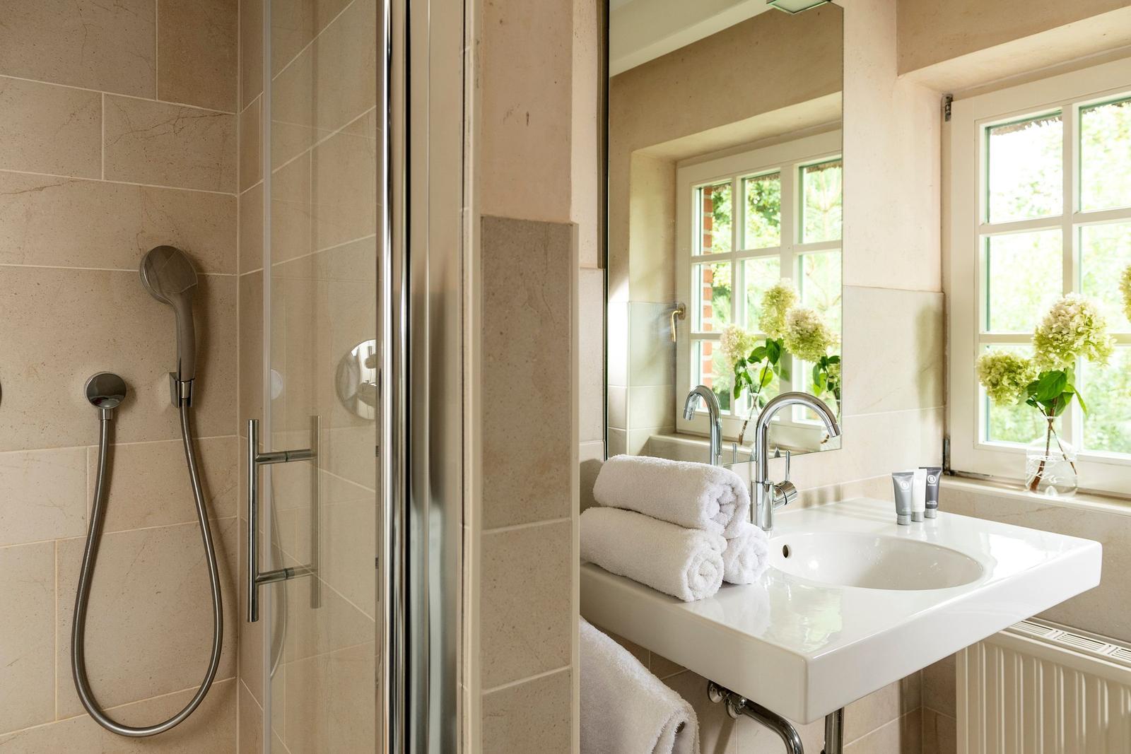 Badezimmer mit Dusche, Waschbecken und Fenster mit Blumen.