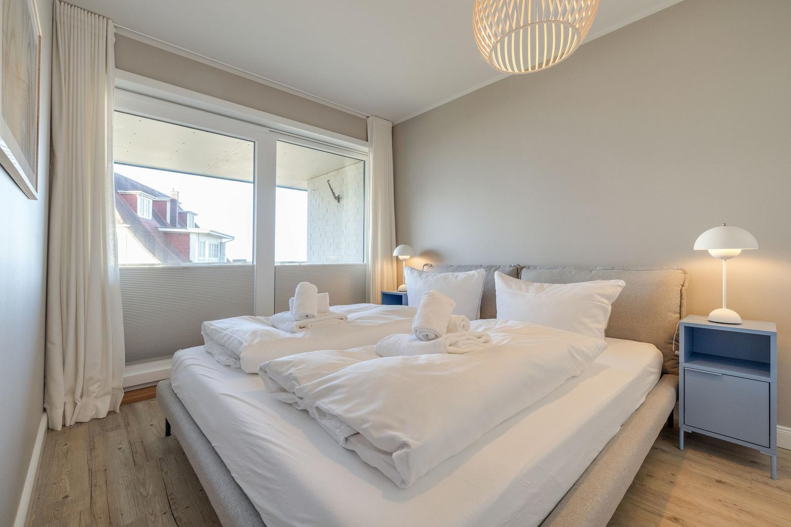 Schlafzimmer mit großem Bett, Fenster und Nachttisch.