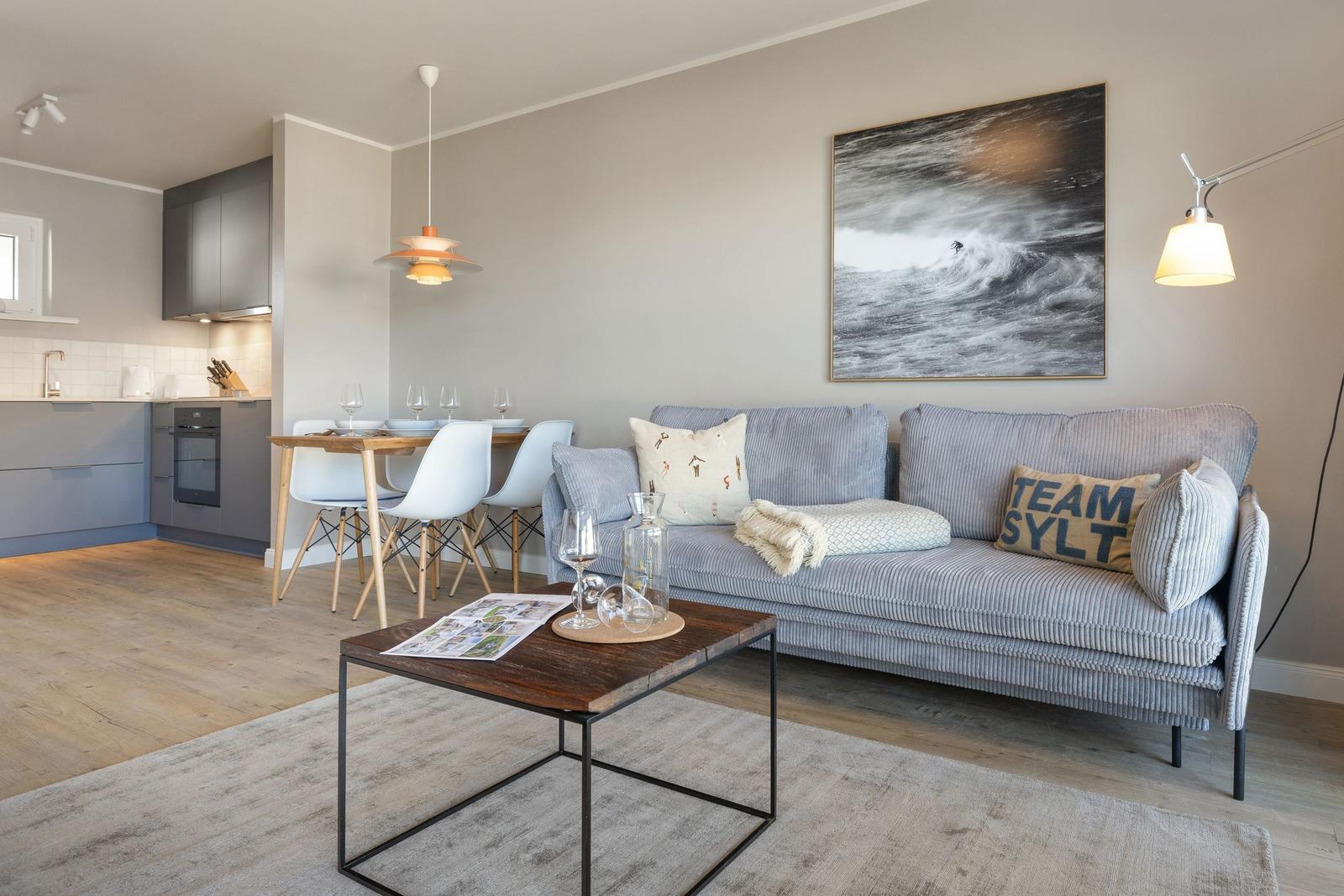 Wohnzimmer mit Sofa, Esstisch und Küchenbereich. Wandbild und Beleuchtung sichtbar.