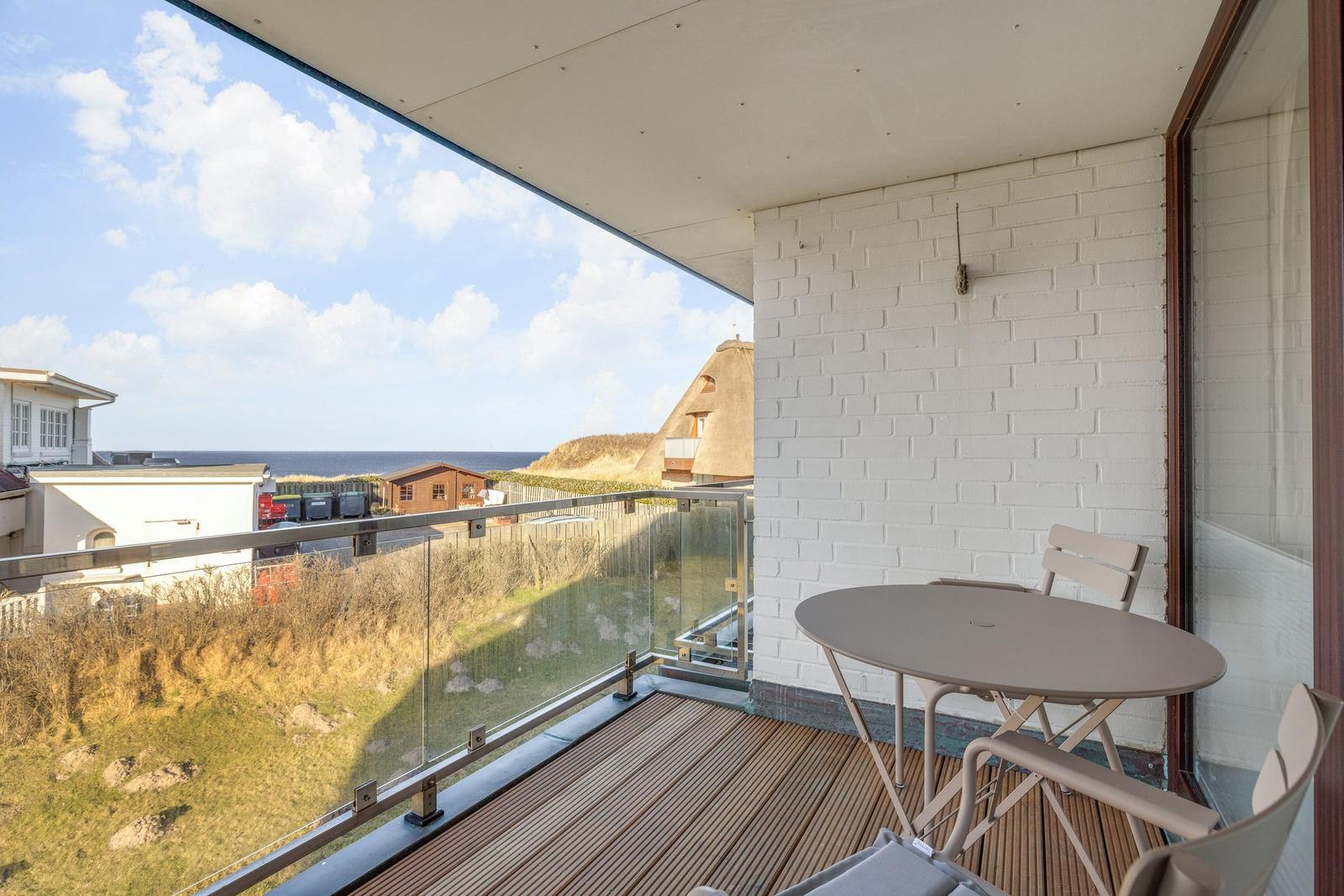 Terrasse mit Tisch und Stühlen, Blick auf Strand und Strandhaus.