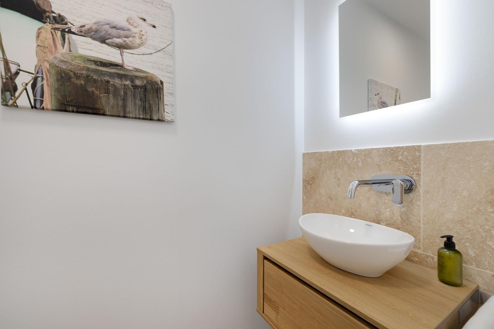 Waschbecken auf Holzschrank mit Spiegel und Wandbild.
