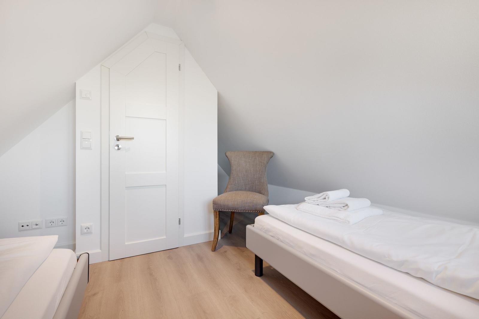 Zimmer mit Doppelbett, Stuhl und Tür unter Dachschräge.