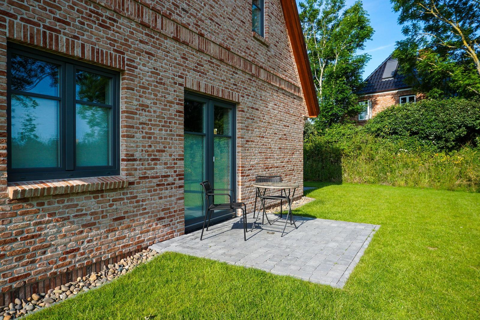 Terrasse mit Tisch und Stühlen vor Backsteinhaus mit Grasfläche