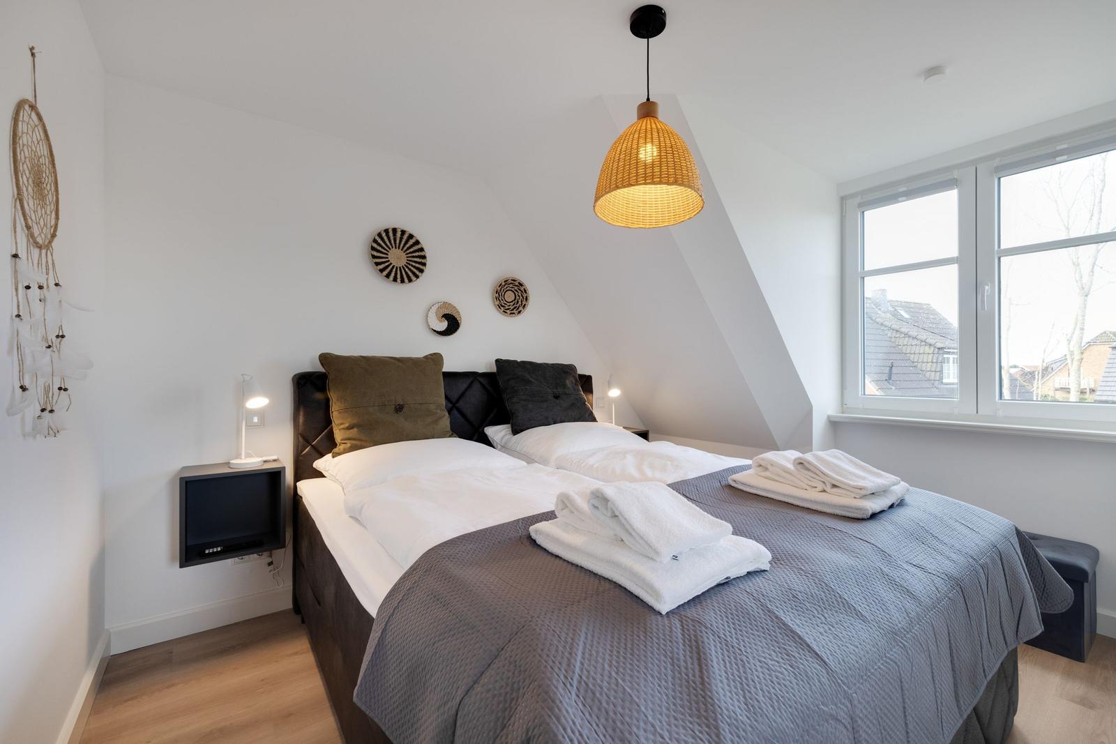 Schlafzimmer mit Doppelbett, Fenster und Deckenleuchte.