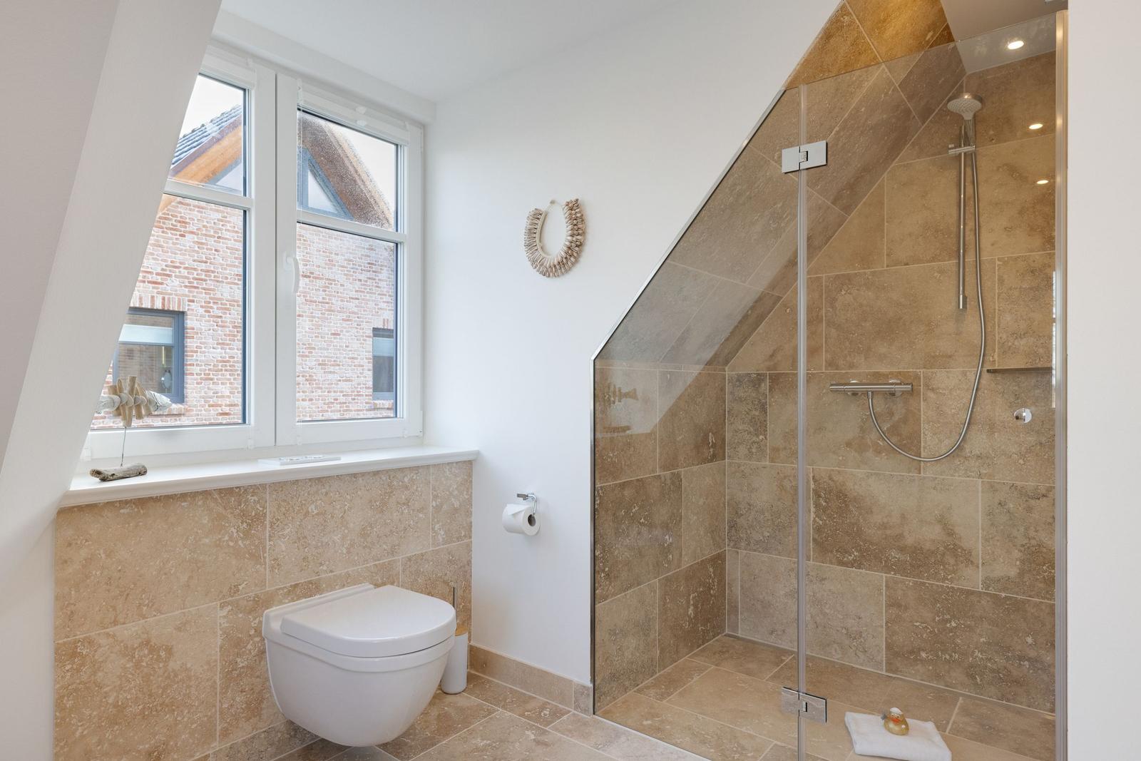 Badezimmer mit Dusche, Toilette und Fenster mit Blick auf Hauswand.