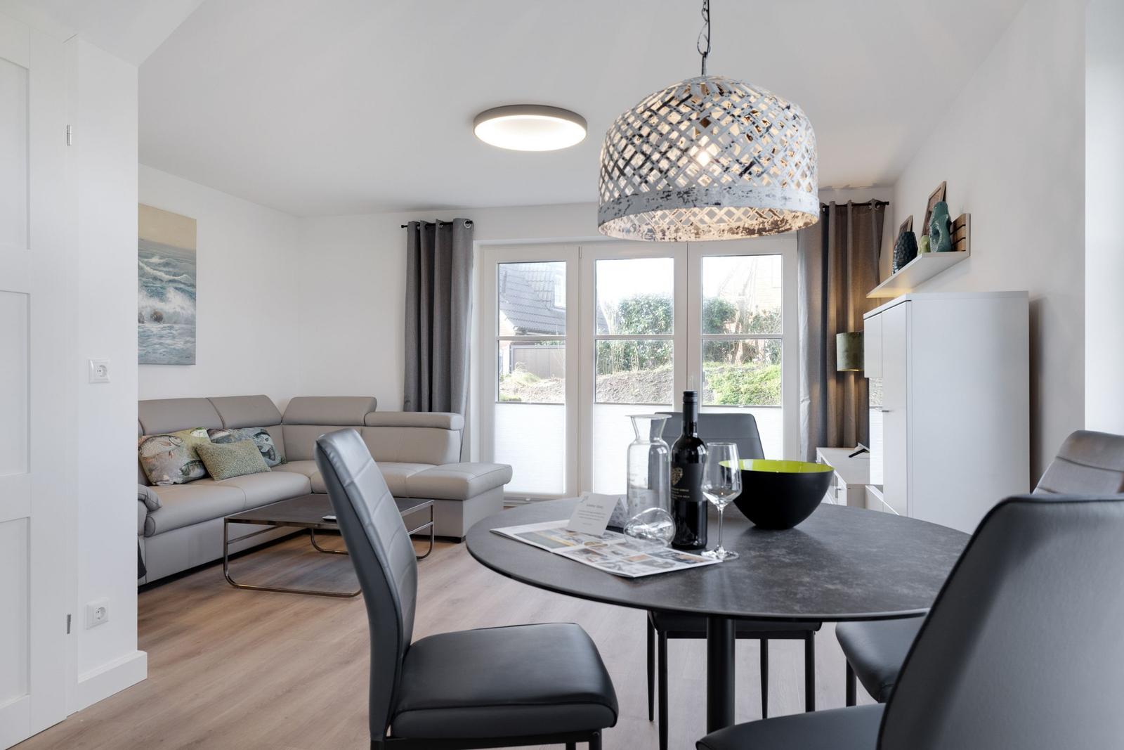Essbereich mit runder Tisch und Stühlen. Wohnbereich mit Sofa und Fenster.