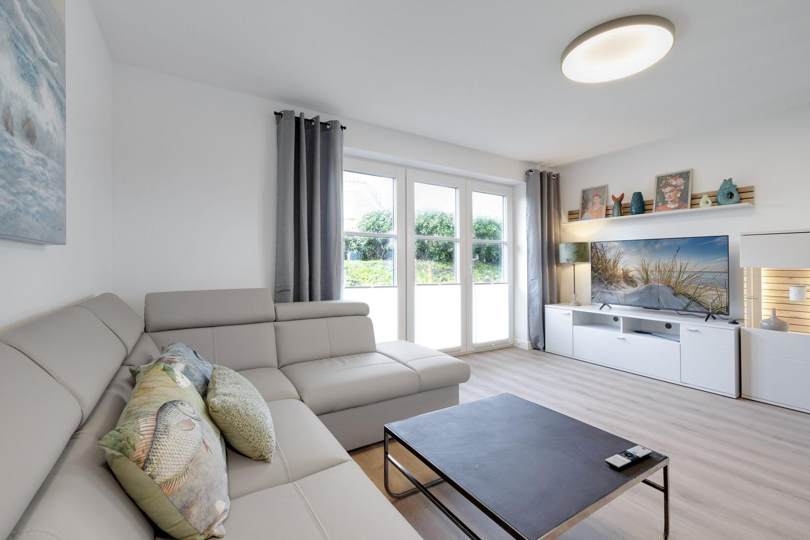 Wohnzimmer mit Sofa, Fernseher und großen Fenstern.