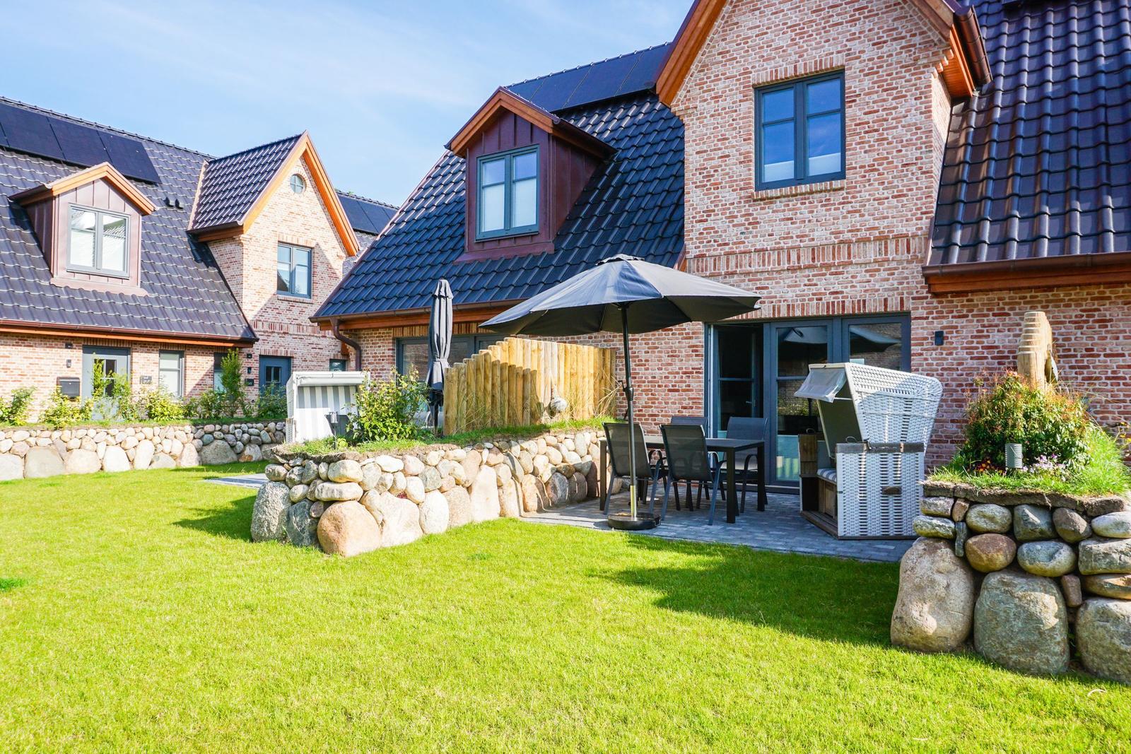Haus mit Steinmauer, Terrasse und Gartenbereich mit Tisch und Sonnenschirm.