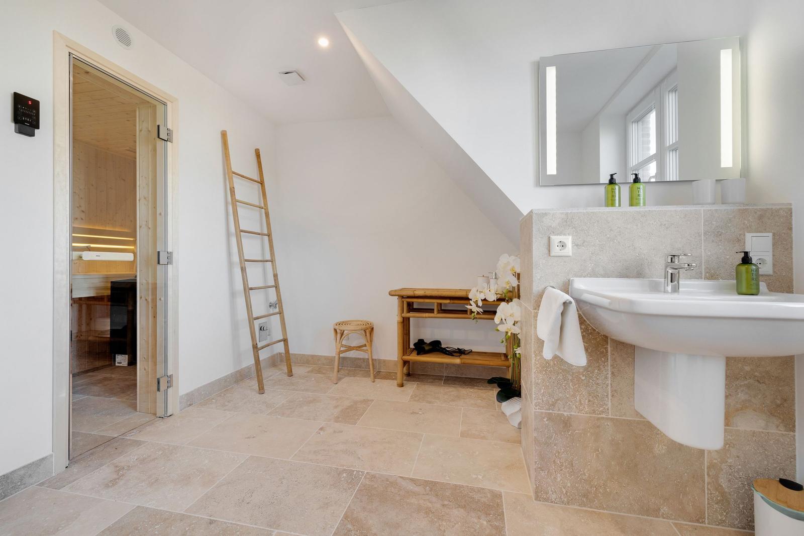 Badezimmer mit Dusche, Waschbecken und Sauna im Hintergrund.