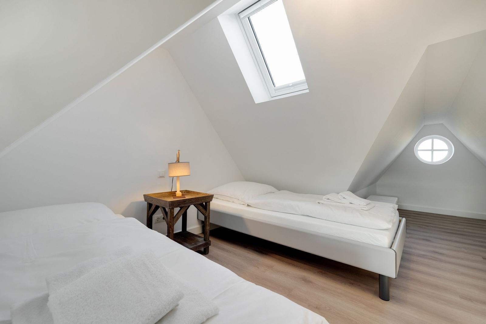 Zwei Betten unter Dachschrägen mit Dachfenster und runden Fenster.
