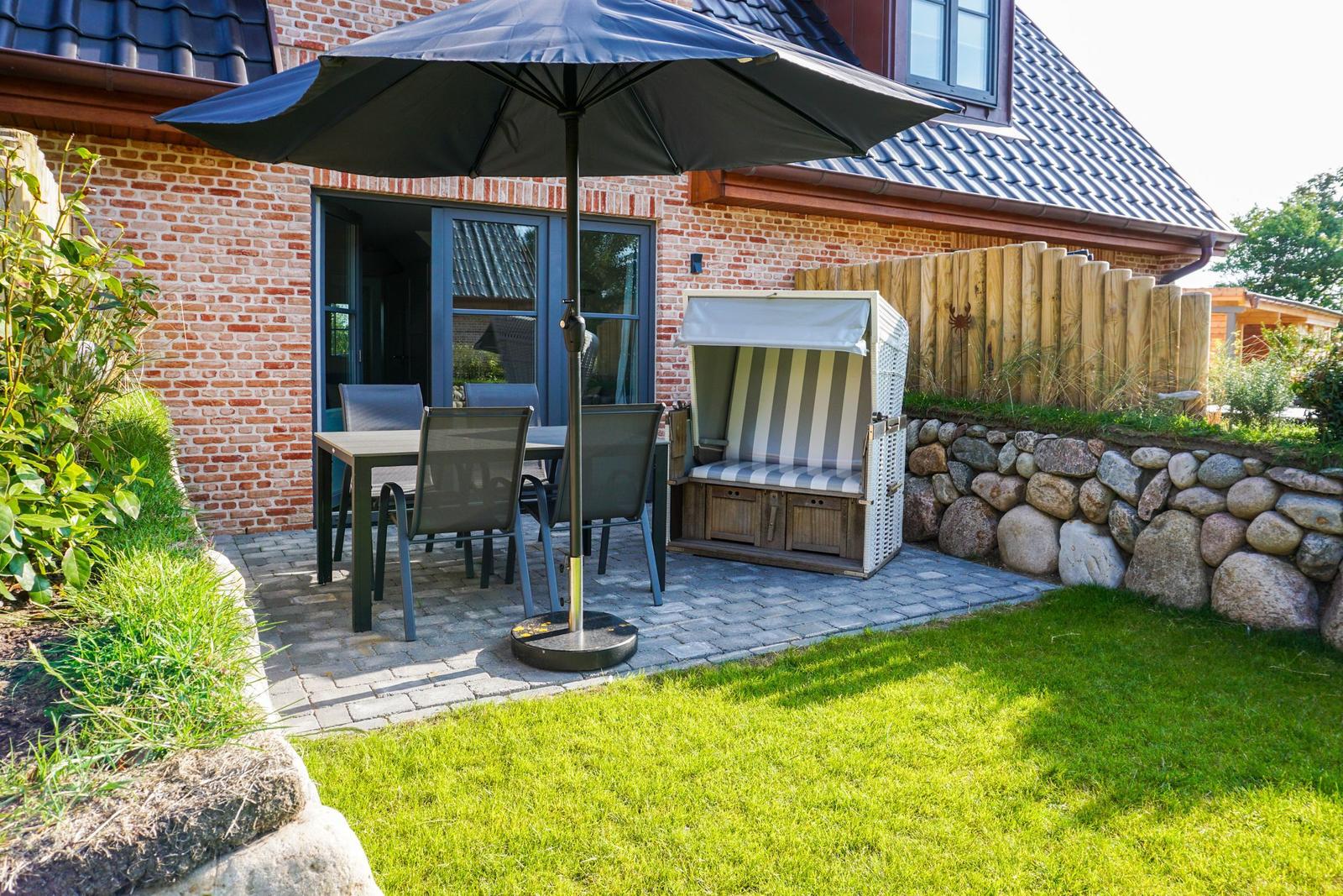 Terrasse mit Tisch, Stühlen und Sonnenschirm neben Strandkorb.