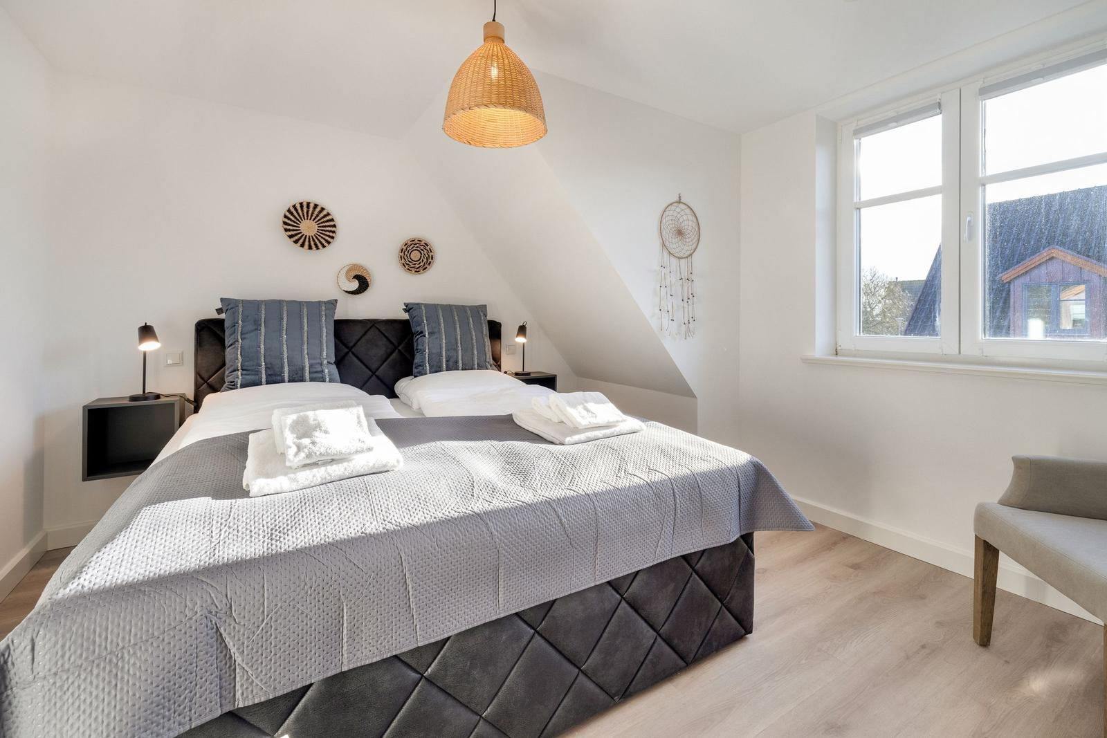 Schlafzimmer mit Doppelbett, Fenster und Deckenleuchte.