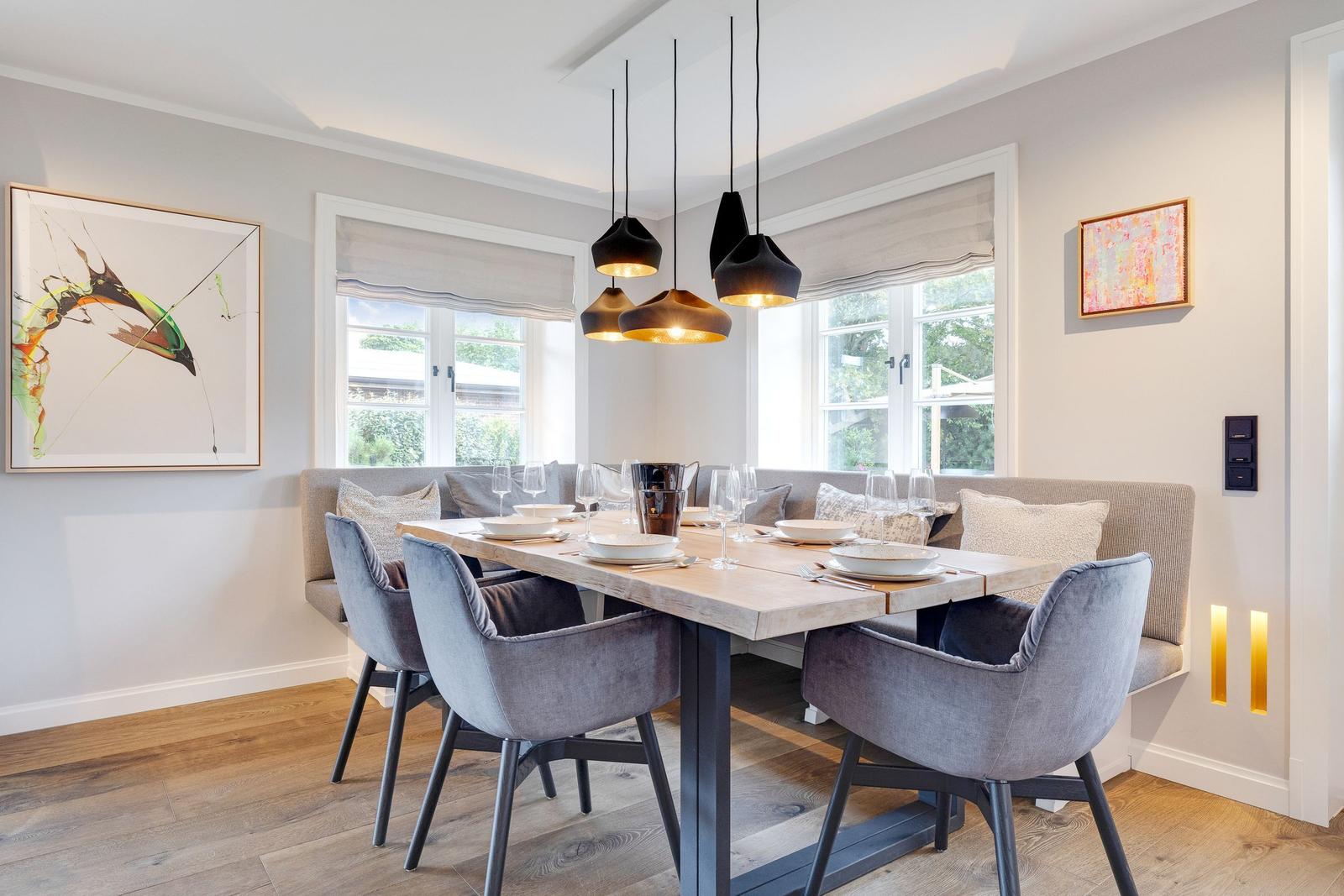 Dining room with wooden table, gray chairs, and windows with view of green.