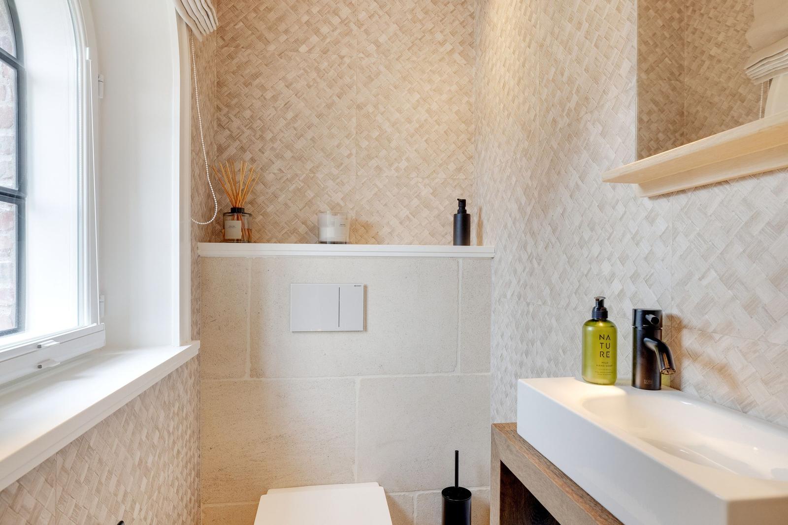 Bathroom with window, sink, and toilet. Walls with woven pattern.