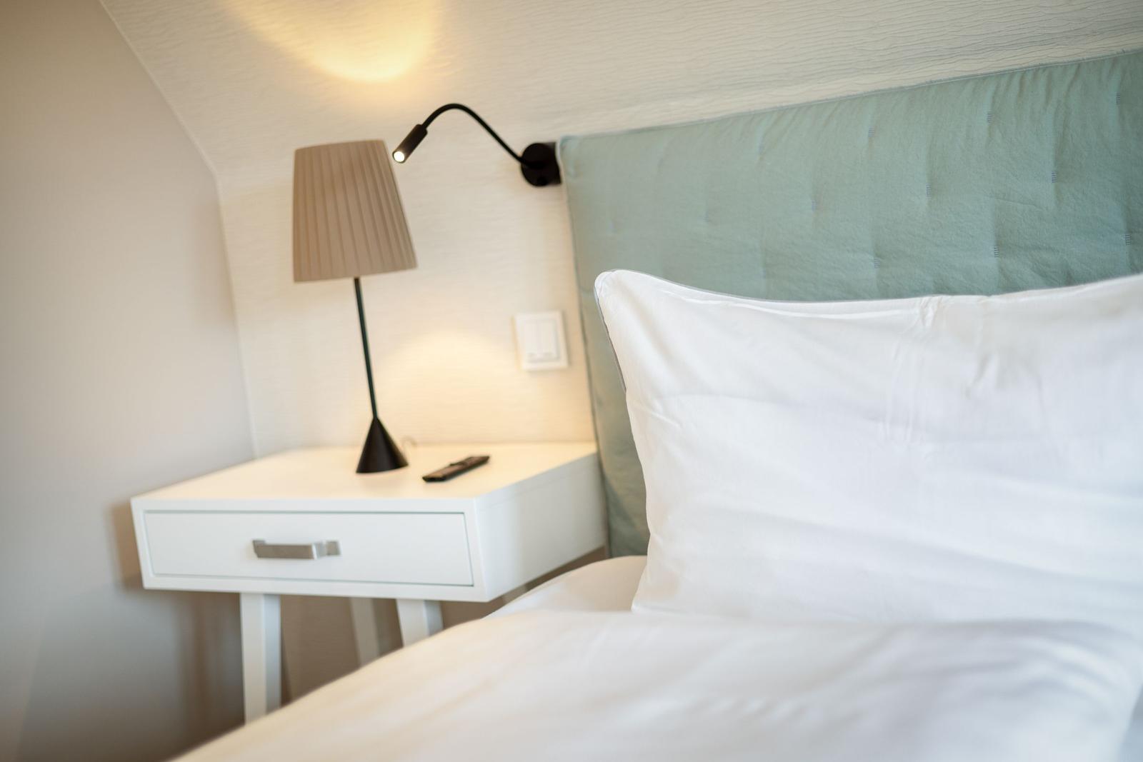 Bed headboard with pillow, nightstand with lamp and remote