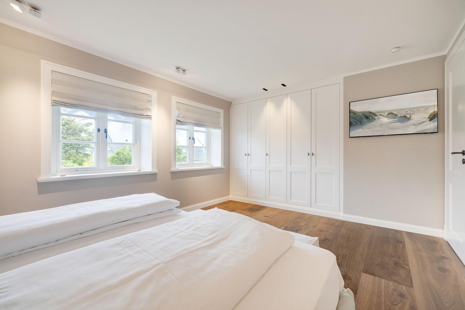 Bedroom with two beds, white closets, and wooden floor.