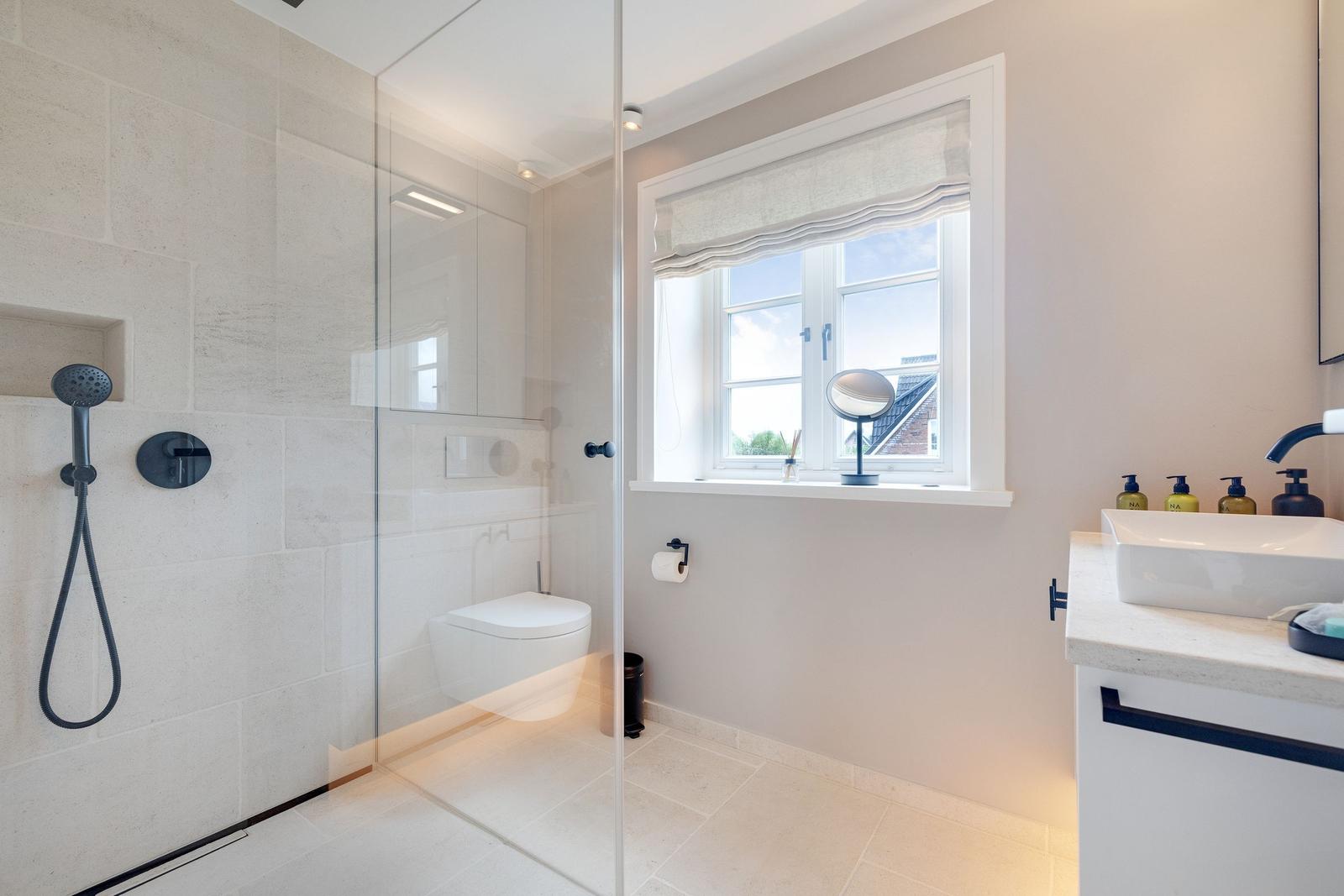 Bathroom with shower, toilet, and sink. Window with roller blind.