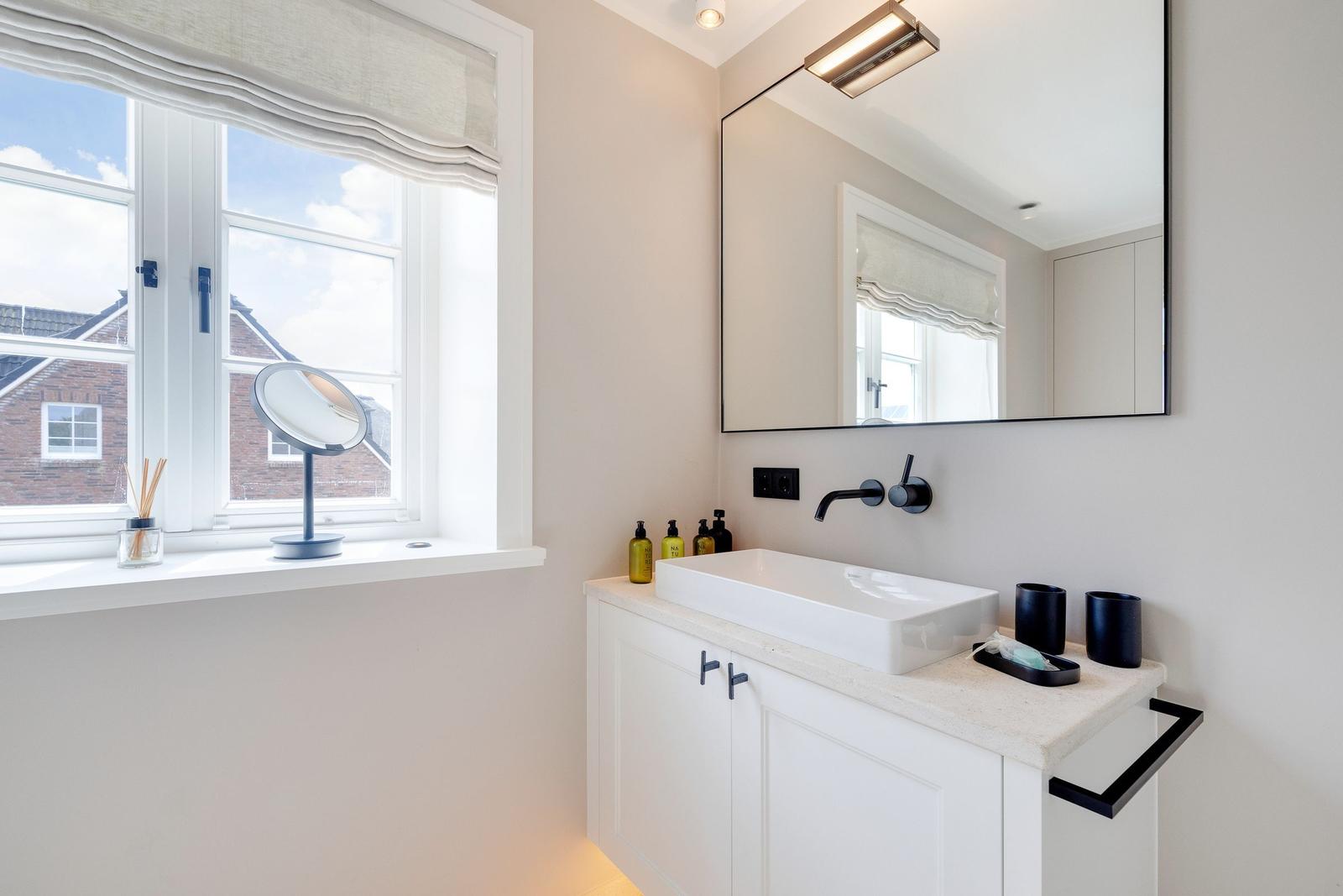 Bathroom with sink, mirror, and window overlooking a house.