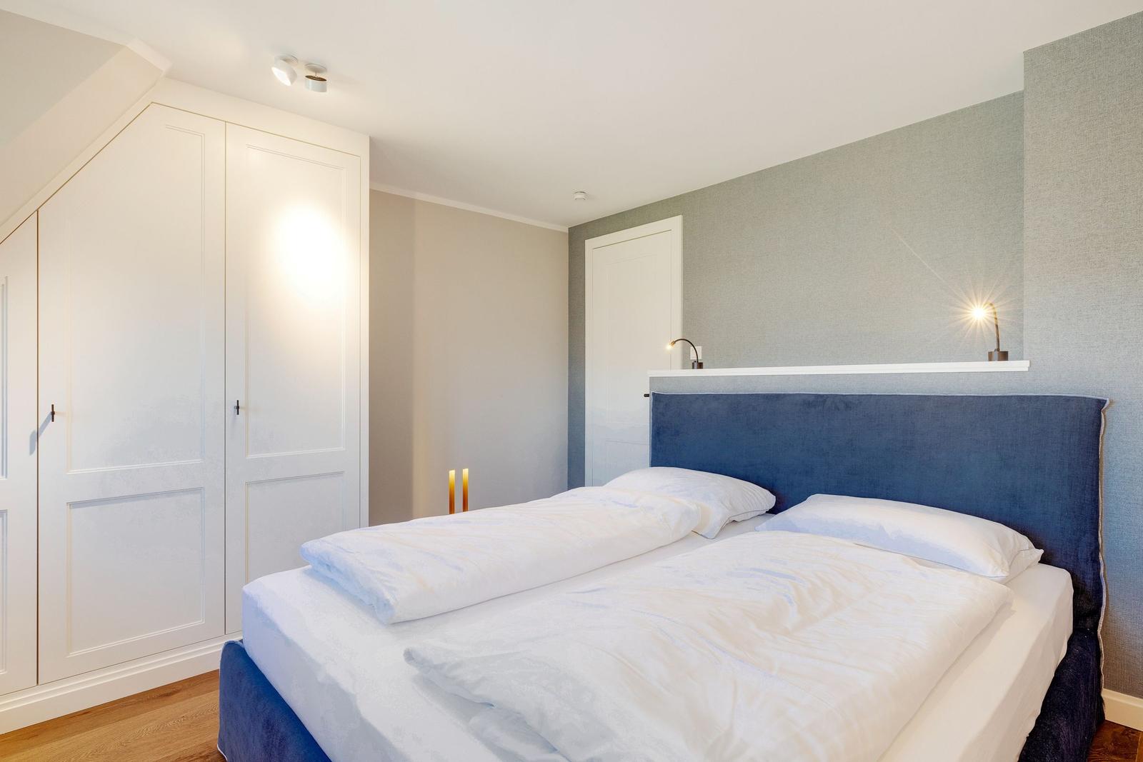 Bedroom with double bed, blue headboard, and white walls.
