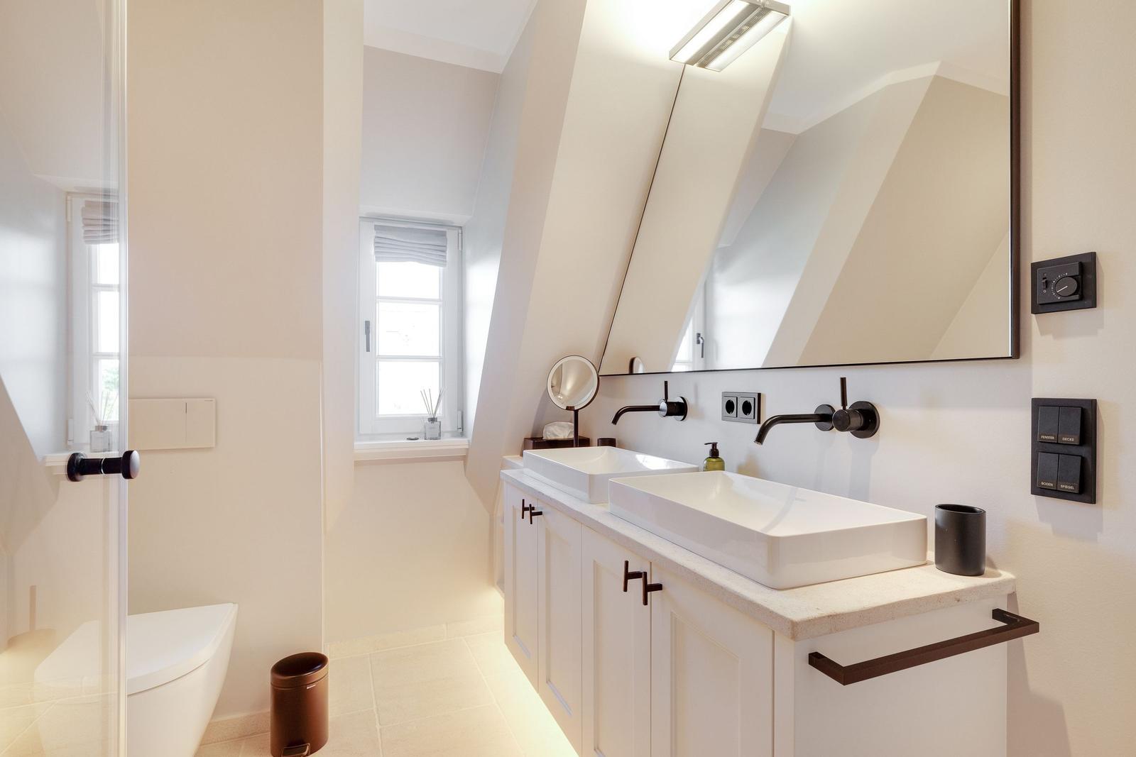 Bathroom with two sinks, mirror, and shower under sloped ceiling.