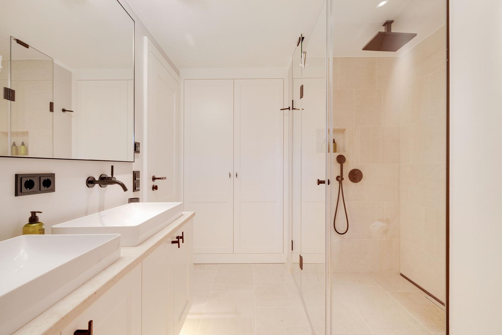 Bathroom with shower, sinks, and mirror cabinet.