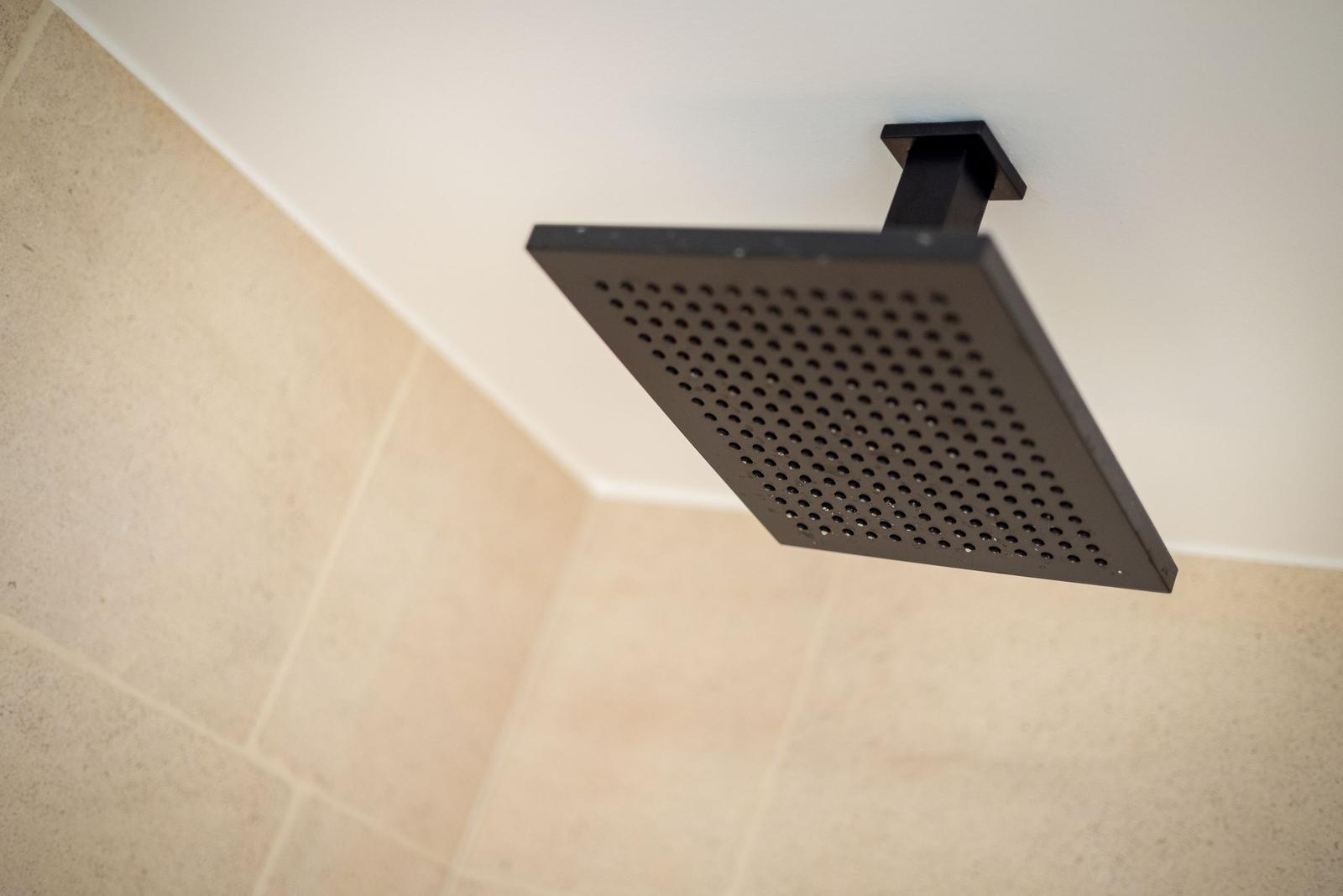 Square shower head with perforated surface mounted on ceiling.