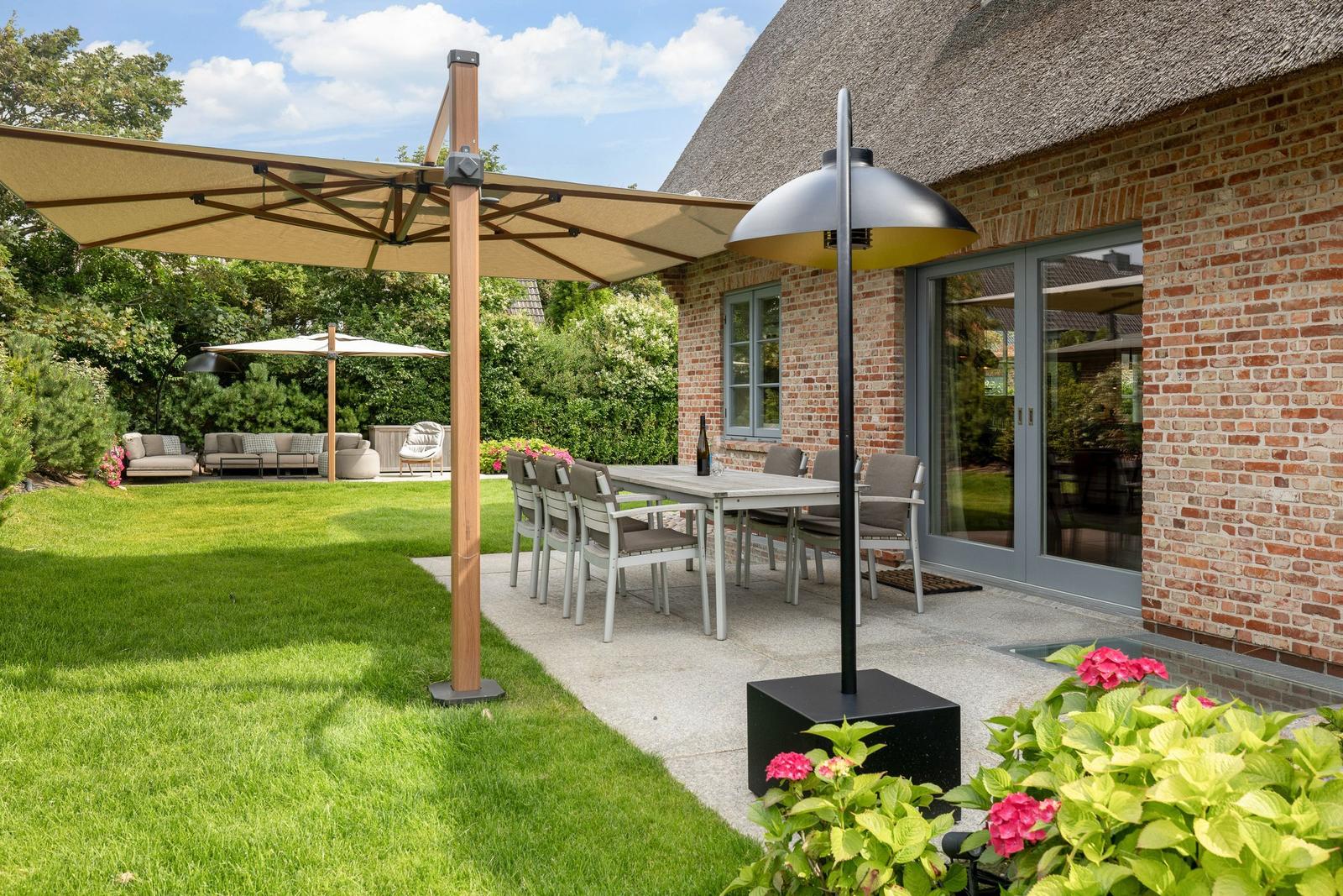Terrace with table, chairs, umbrella, and garden house. Lawn and flowers in foreground.