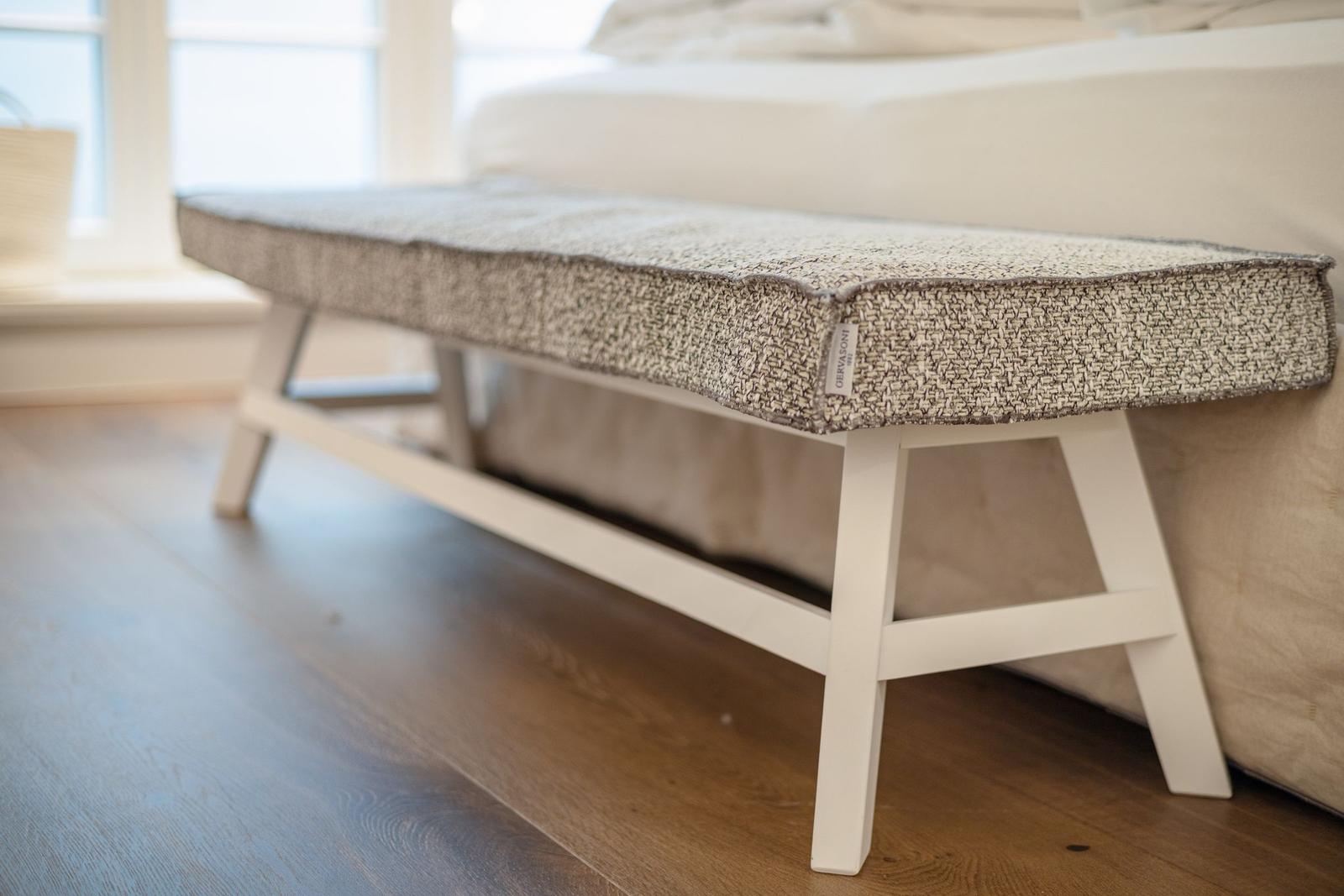 A white bench with patterned upholstery is placed at the foot of a bed.