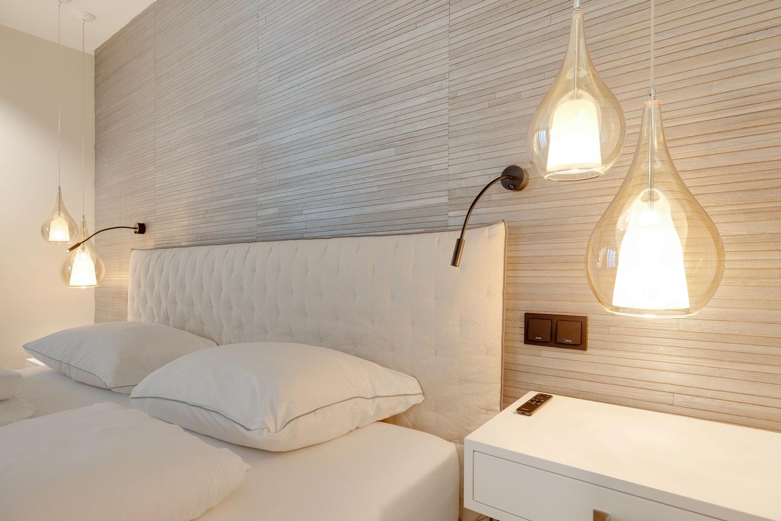 Bedroom with white bed, wood wall, and hanging lamps.