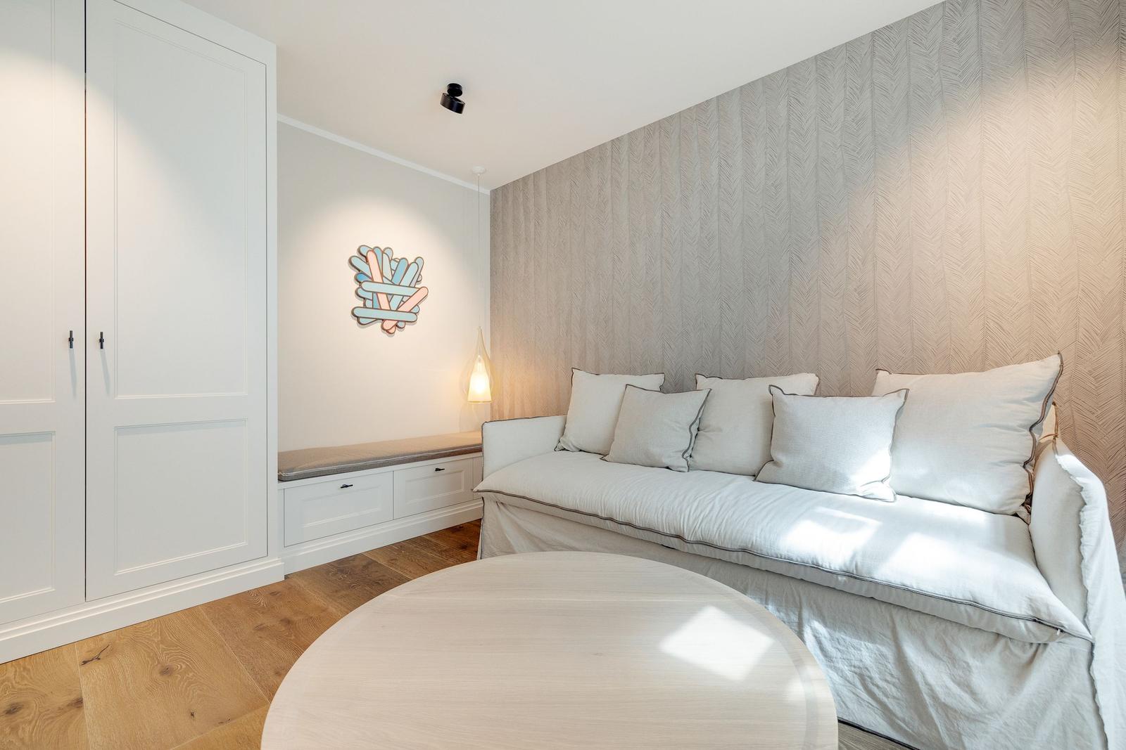 A room with sofa, round table, and white cabinets against the wall.