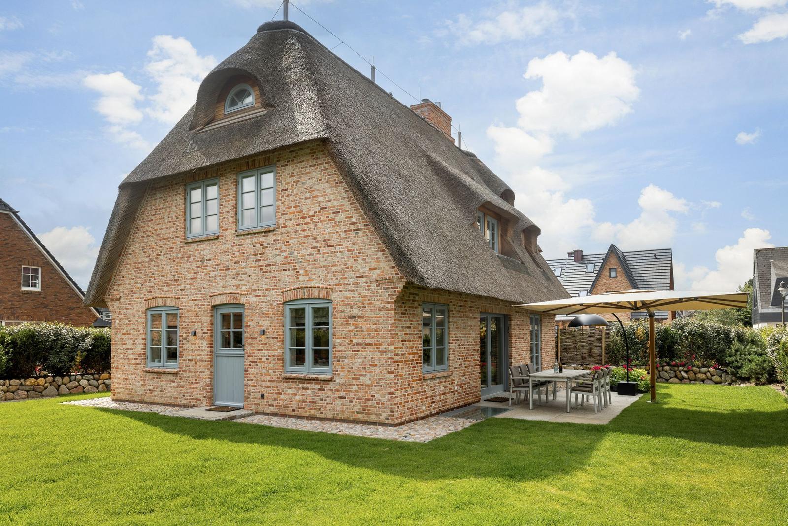 House with thatched roof and garden with table and umbrella.