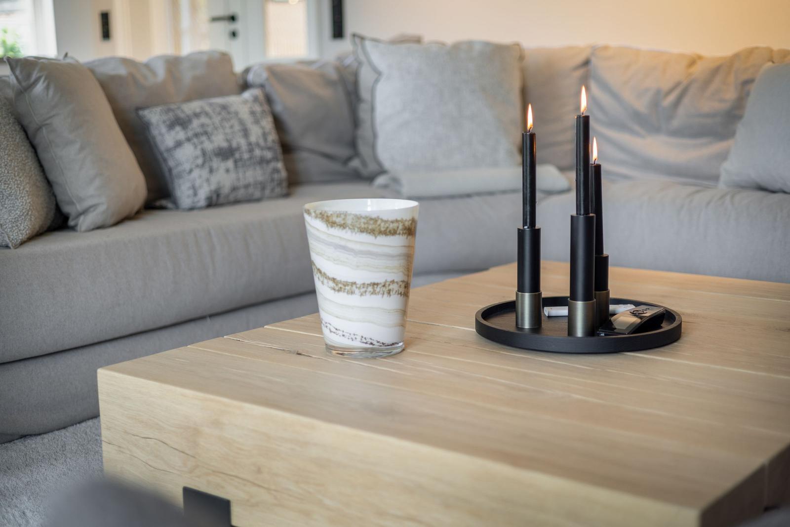 Wooden table with cup and lit candles in front of a sofa.