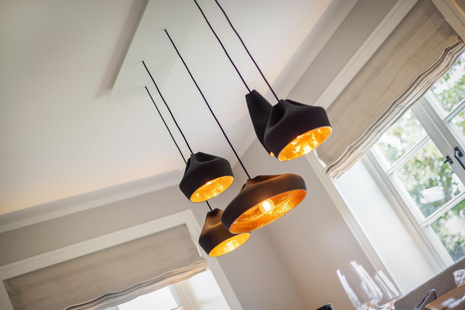 Suspended lamp with four black-golden shades over a dining area with window.
