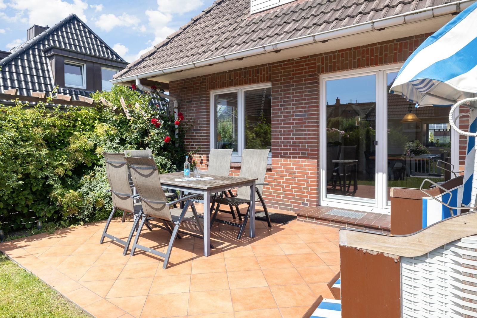 Terrasse mit Tisch, Stühlen und Sonnenschirm neben Haus mit Schiebetür.