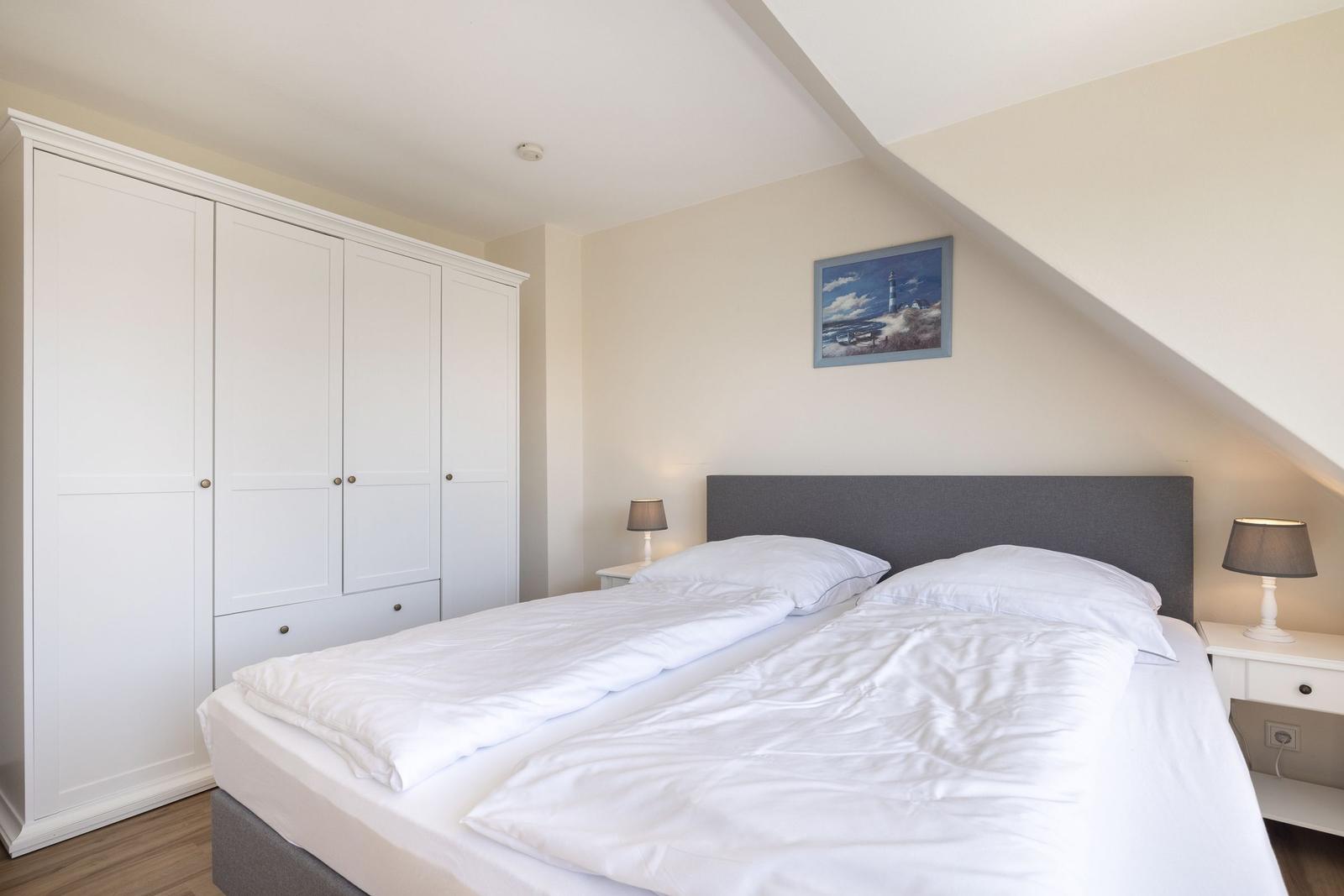 Schlafzimmer mit Doppelbett, weißen Schränken und Nachttischen unter schrägem Dach.