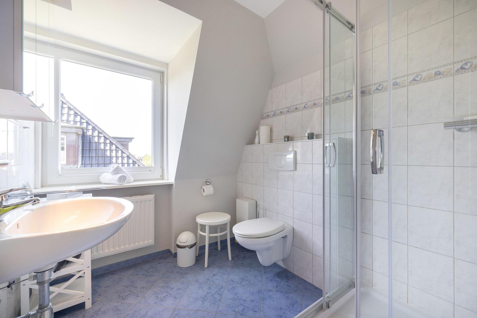 Badezimmer mit Dusche, Toilette und Waschbecken unter Fenster.