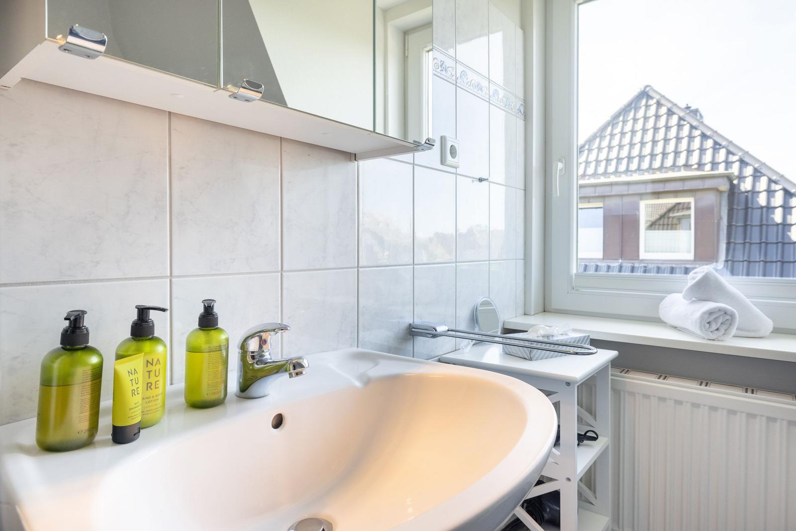 Bad mit Waschbecken, Spiegel und Fensterblick auf Dach.