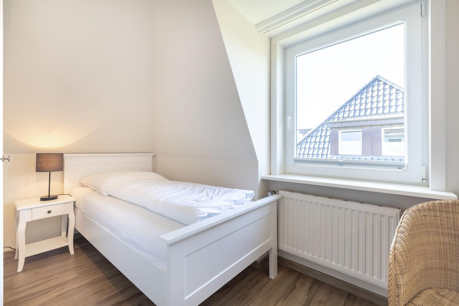 Ein Schlafzimmer mit weißem Bett, Nachttisch und Fenster mit Blick auf ein Haus.