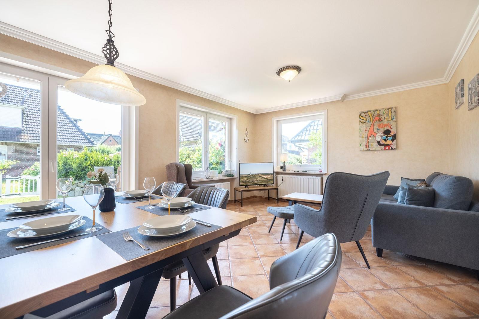 Essbereich mit Tisch und Stühlen, Wohnbereich mit Sofa und Fernseher, Fenster mit Blick auf Garten.