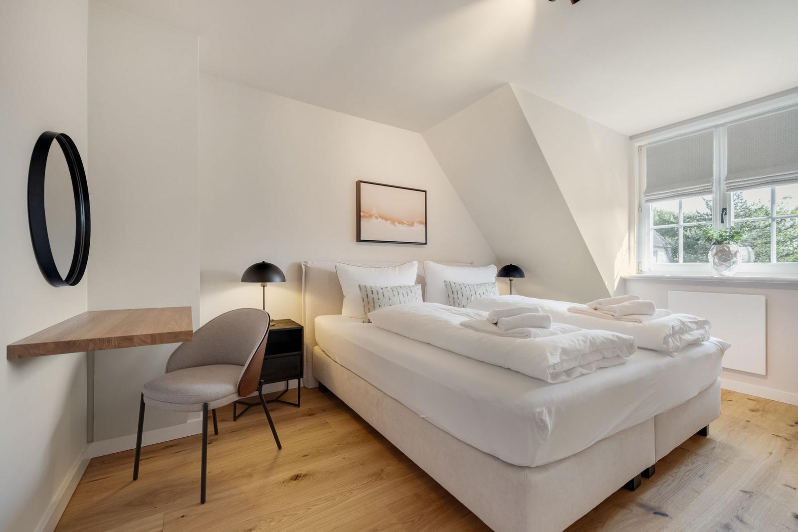 Schlafzimmer mit Doppelbett, Schreibtisch und Fenster mit Blick auf Grün.