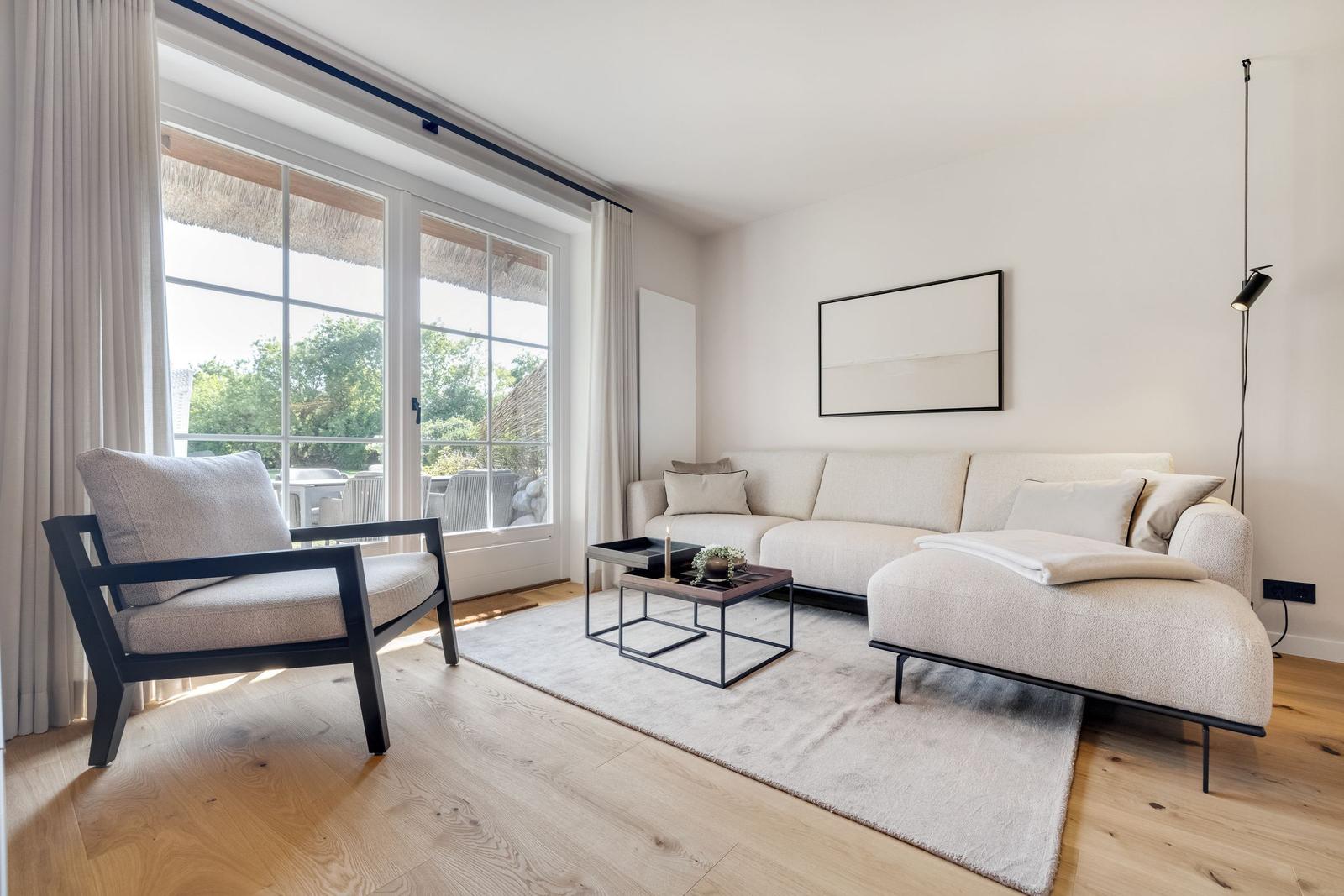 Wohnzimmer mit Sofa, Sessel und Tisch vor großem Fenster