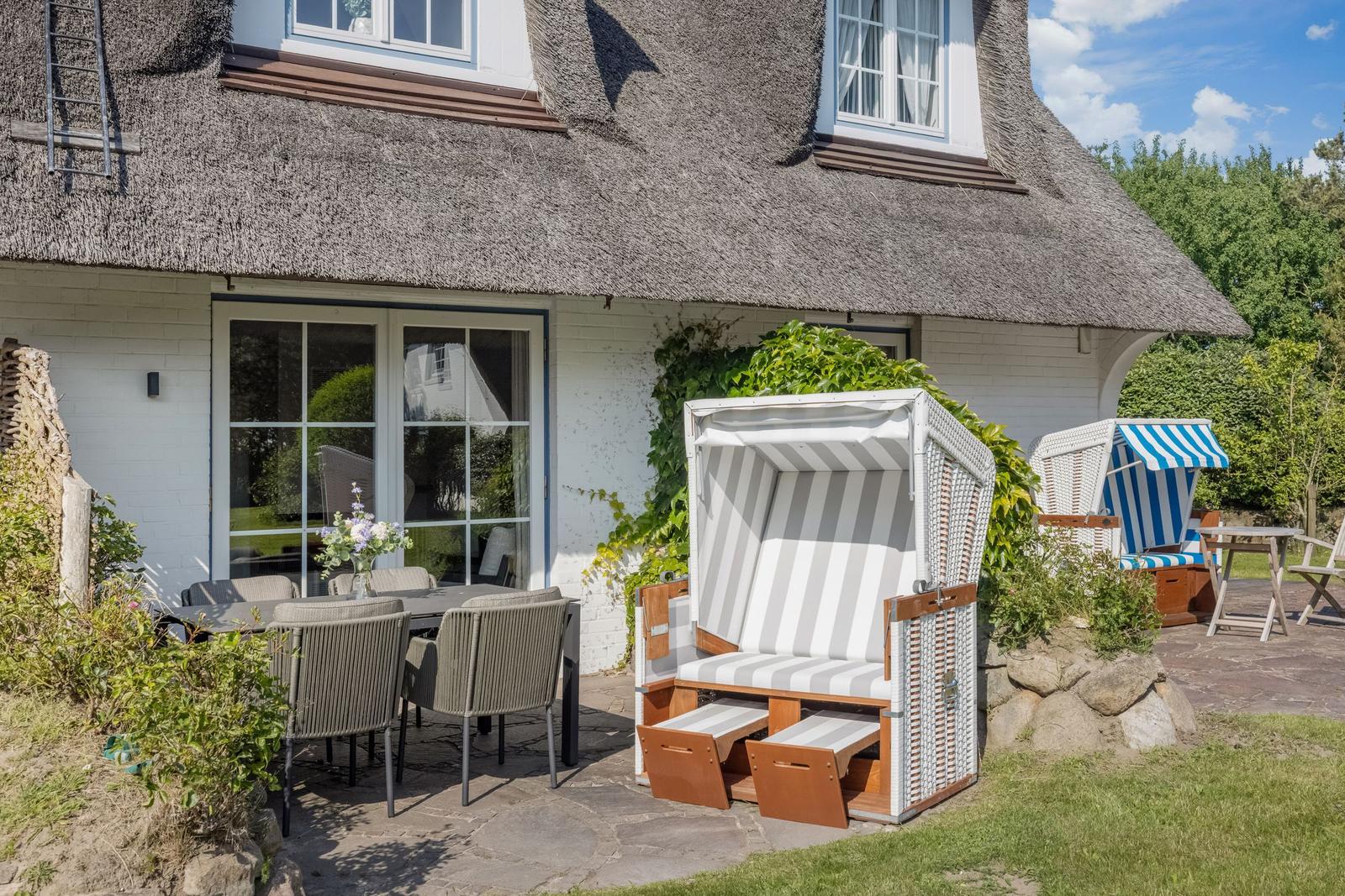 Haus mit Strohdach, Terrasse mit Esstisch, Strandkörben und Garten.