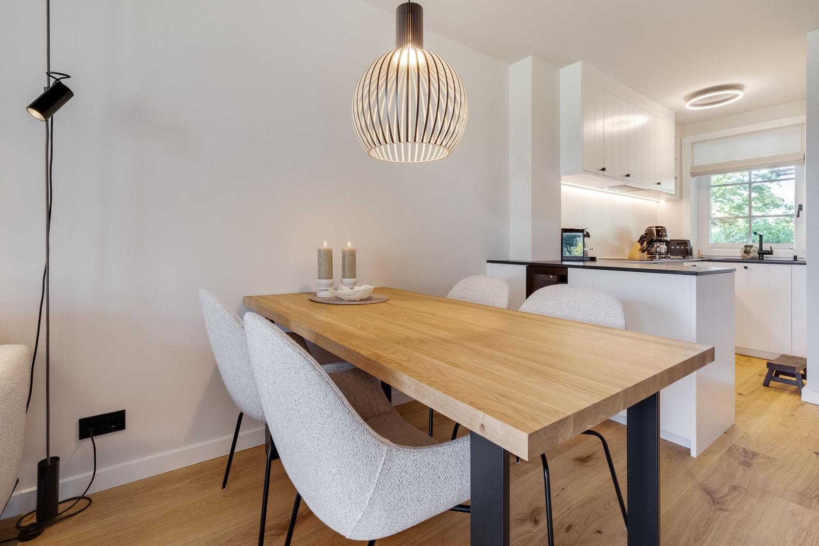 Essbereich mit Holztisch, Stühlen und Deckenleuchte. Küche mit Arbeitsplatte und Fenster.