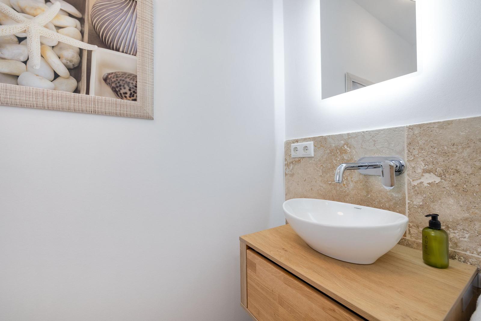 Waschbecken auf Holzunterschrank mit Spiegelschrank und Wandbild mit Muscheln.