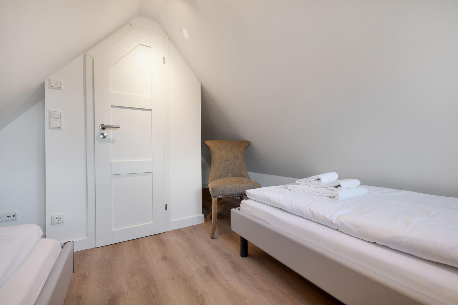 Schlafzimmer mit Dachschrägen, Bett, Stuhl und Tür.