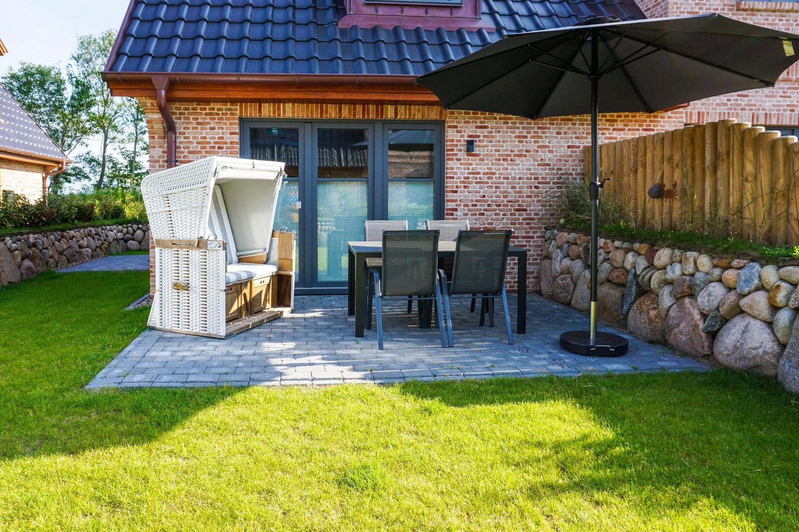 Terrasse mit Sitzgruppe, Sonnenschutz und Strandkorb vor Haus mit Backsteinmauer.