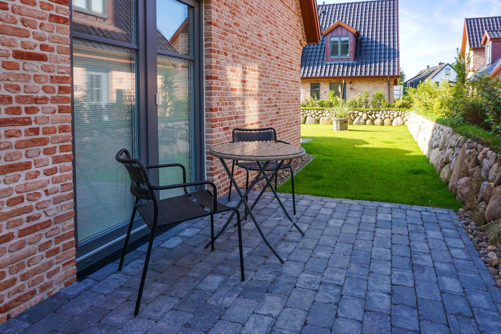 Terrasse mit Tisch und Stühlen neben Backsteinhaus mit Garten.