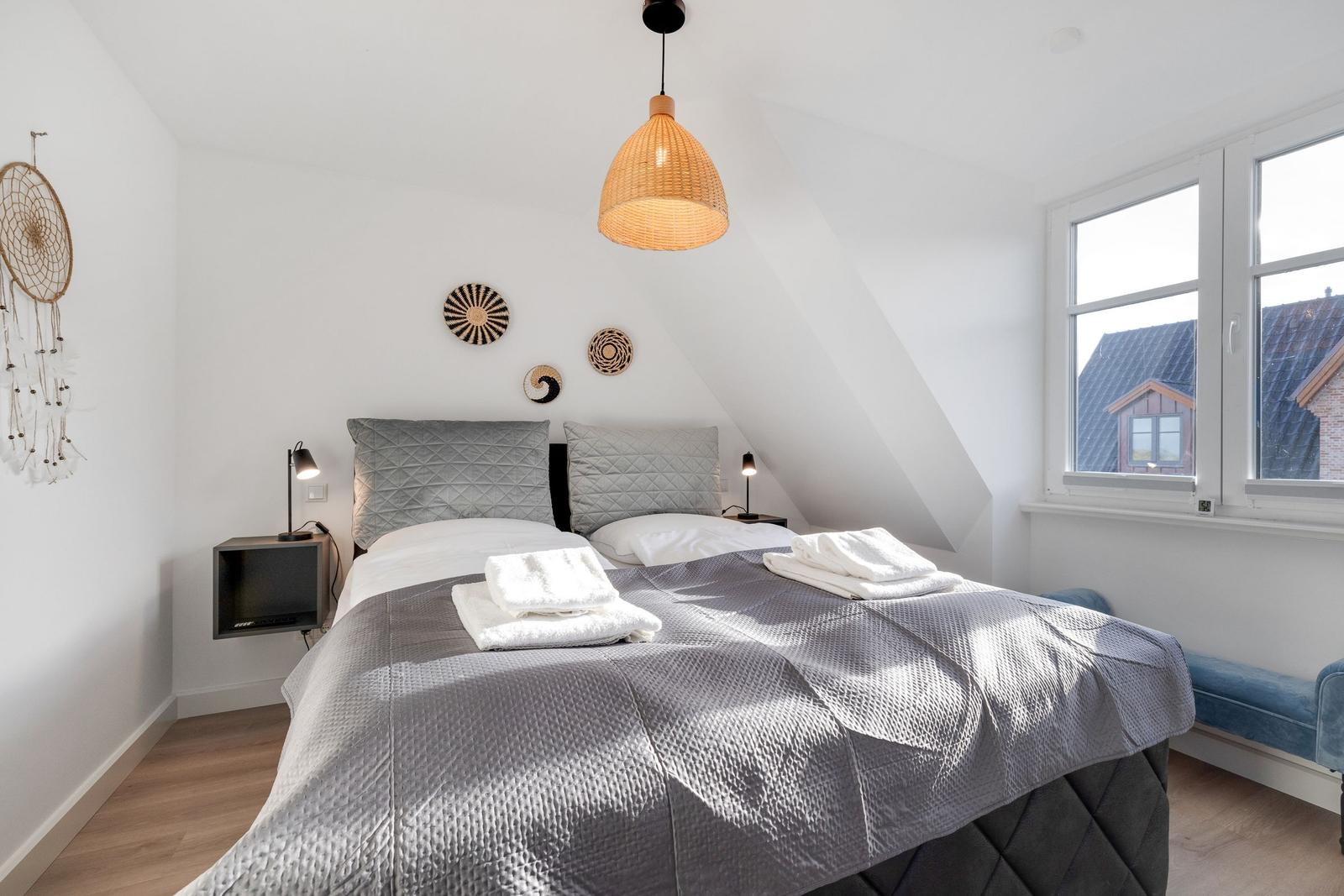 Schlafzimmer mit Doppelbett, Fenster und Deckenleuchte.